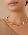 Close-up of a woman wearing a gold necklace and earrings against a beige background