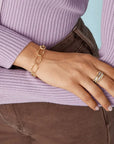 Person wearing a gold bracelet and ring on a light blue background