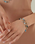 Close-up of hands wearing gold ring and beaded bracelet on a neutral background