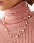 Necklace with multicolored beads worn by a person in a pink turtleneck.