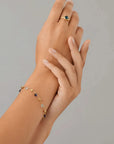 Hand wearing a gold bracelet with small beads on a gray background
