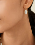 Close-up of a woman wearing pearl earrings with a neutral background