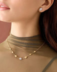 Close-up of a woman wearing gold jewelry including earrings and a necklace on a brown background