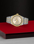 Two-tone watch with silver and gold accents on a red platform against a black background