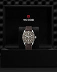 Tudor watch with brown leather strap in a black box on a textured black background