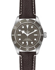 Tudor watch with black dial and brown leather strap on a white background