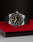 Tudor Watch with black strap and silver case on a red platform against a dark background
