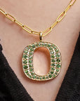 Gold chain necklace with a large open letter 'O' pendant encrusted with green gemstones, shown worn on a person's neck.