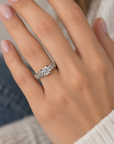 A close-up of a person's hand wearing a silver-toned diamond ring with a round-cut center stone and smaller diamonds along the band.
