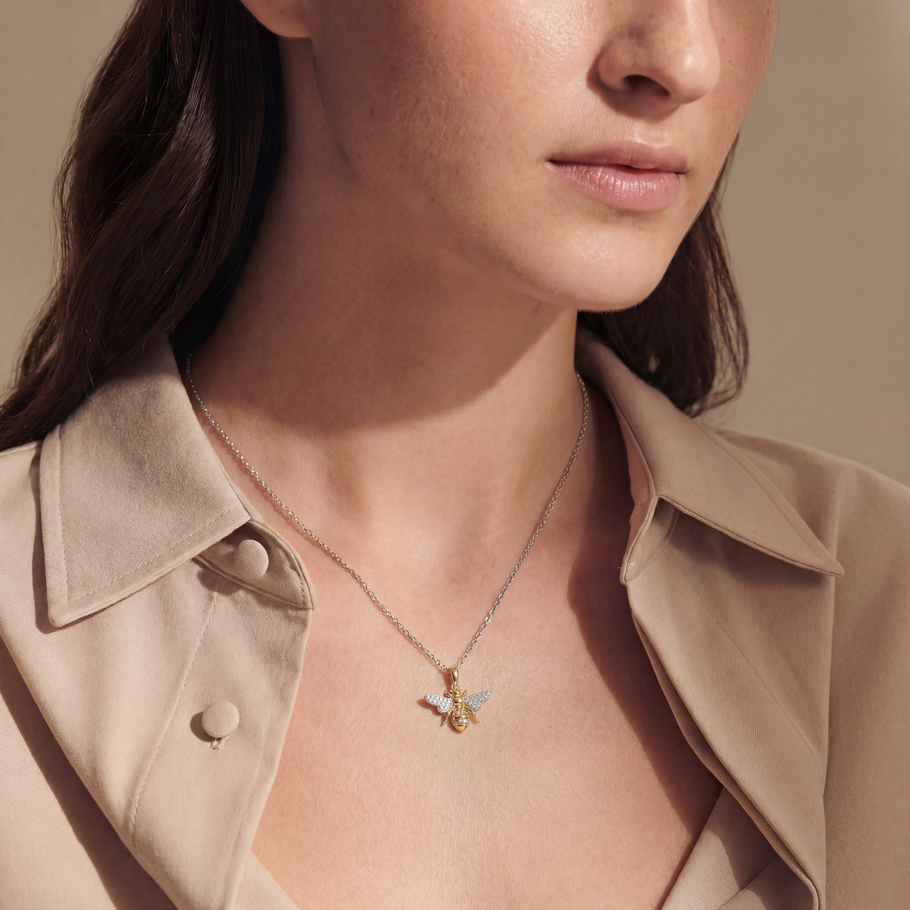 Close-up of a woman wearing a necklace with a bee pendant, set against a neutral background.