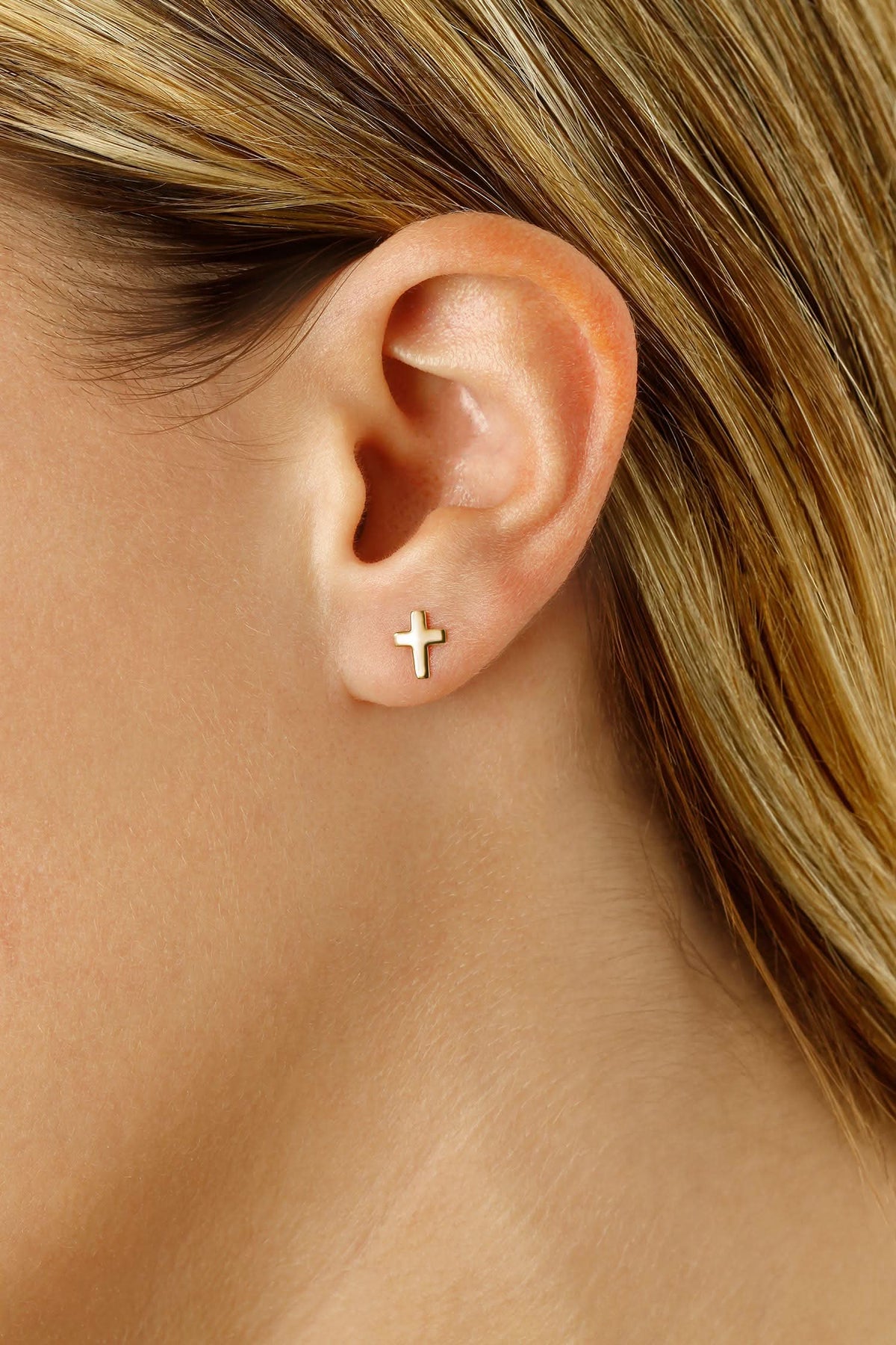Close-up of an ear wearing a gold cross earring with blonde hair.