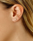Close-up of an ear wearing a gold cross earring with blonde hair.