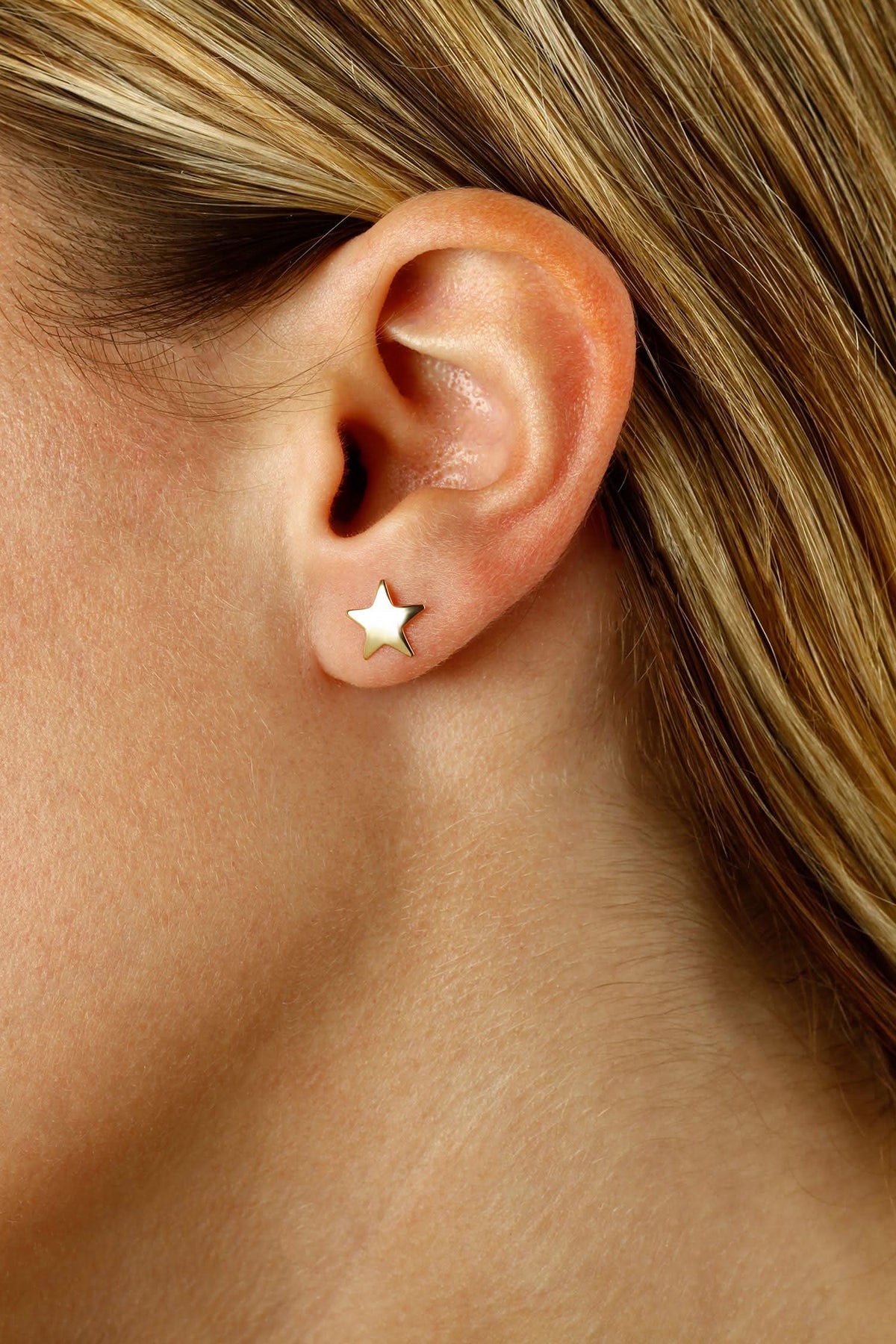 A close-up of a person's ear wearing a small gold star stud earring.