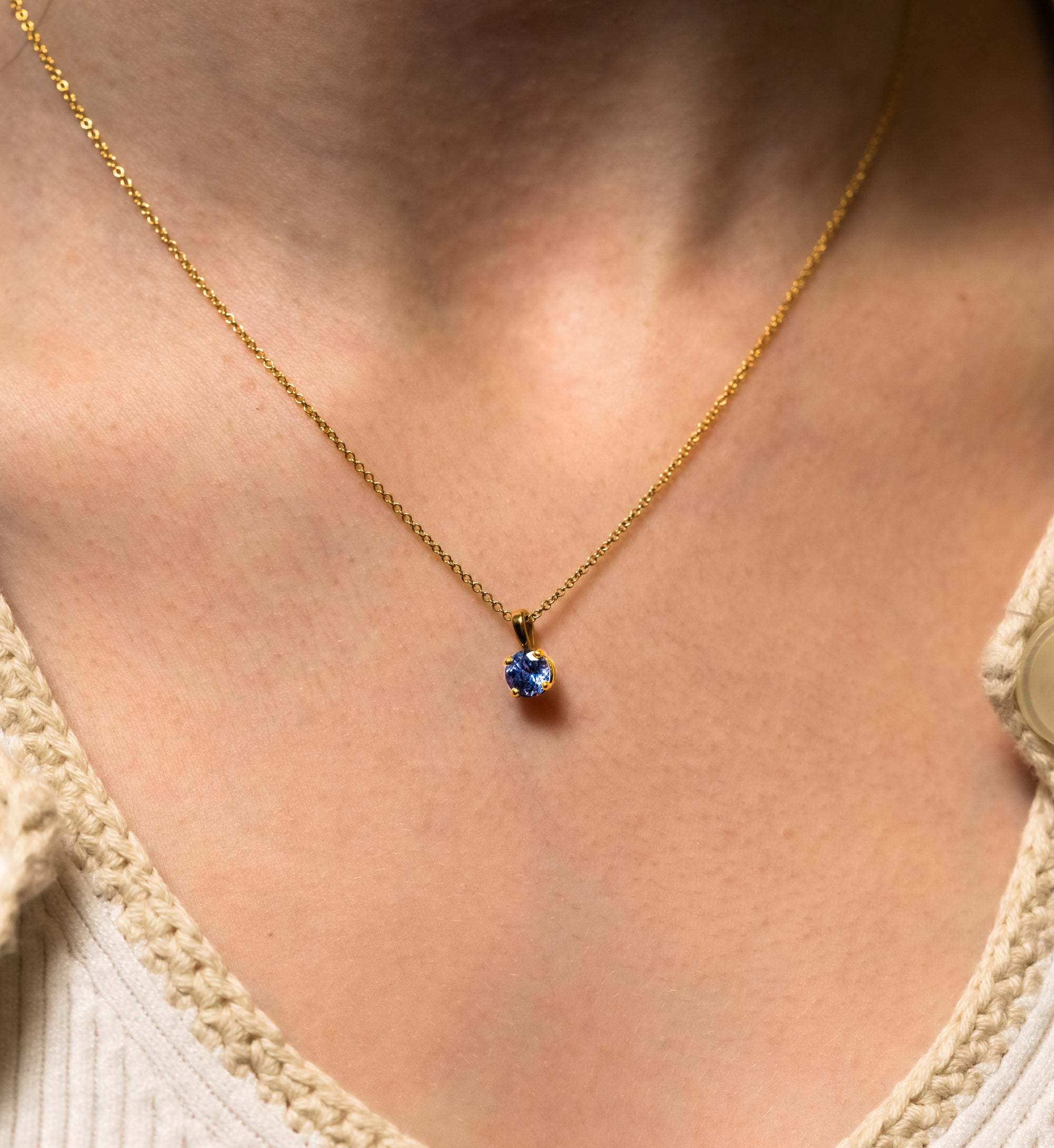 a blue tanzanite pendant on a gold chain worn by a person close-up view.