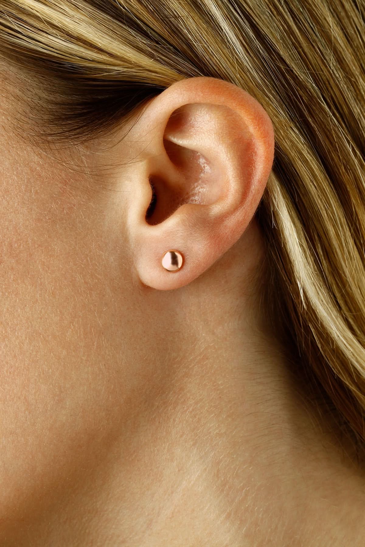 A close-up of a person's ear wearing a small polished rose gold stud earring.