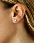 A close-up of a person's ear wearing a small polished rose gold stud earring.