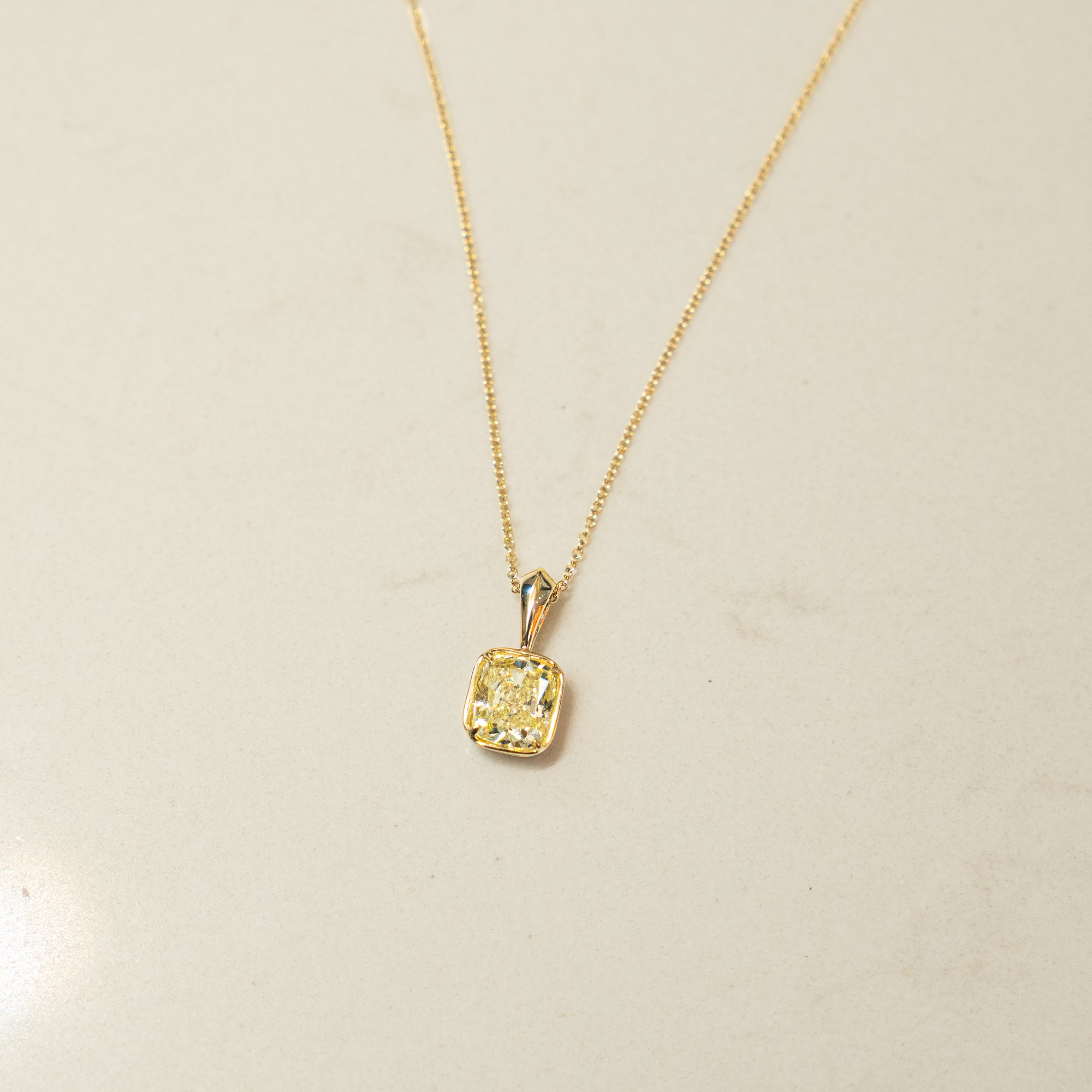 Gold necklace with a square pendant with yellow diamond center on a beige background