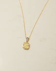 Gold necklace with a square pendant with yellow diamond center on a beige background