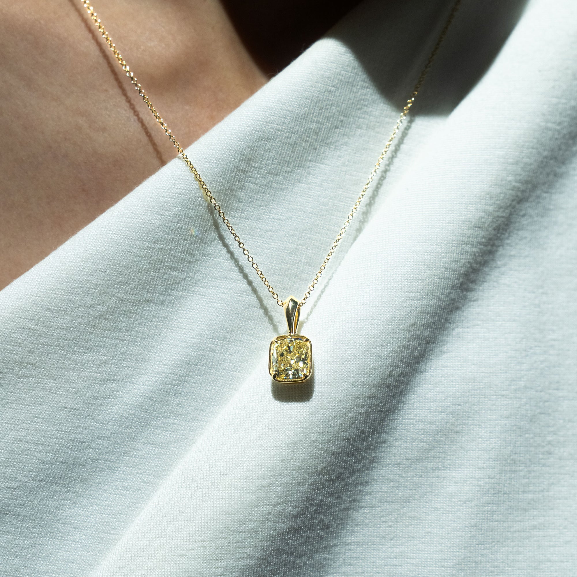 person wearing a gold necklace with a yellow gemstone pendant on a white fabric background
