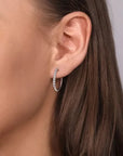 Close-up of a woman wearing silver hoop earrings with a neutral background