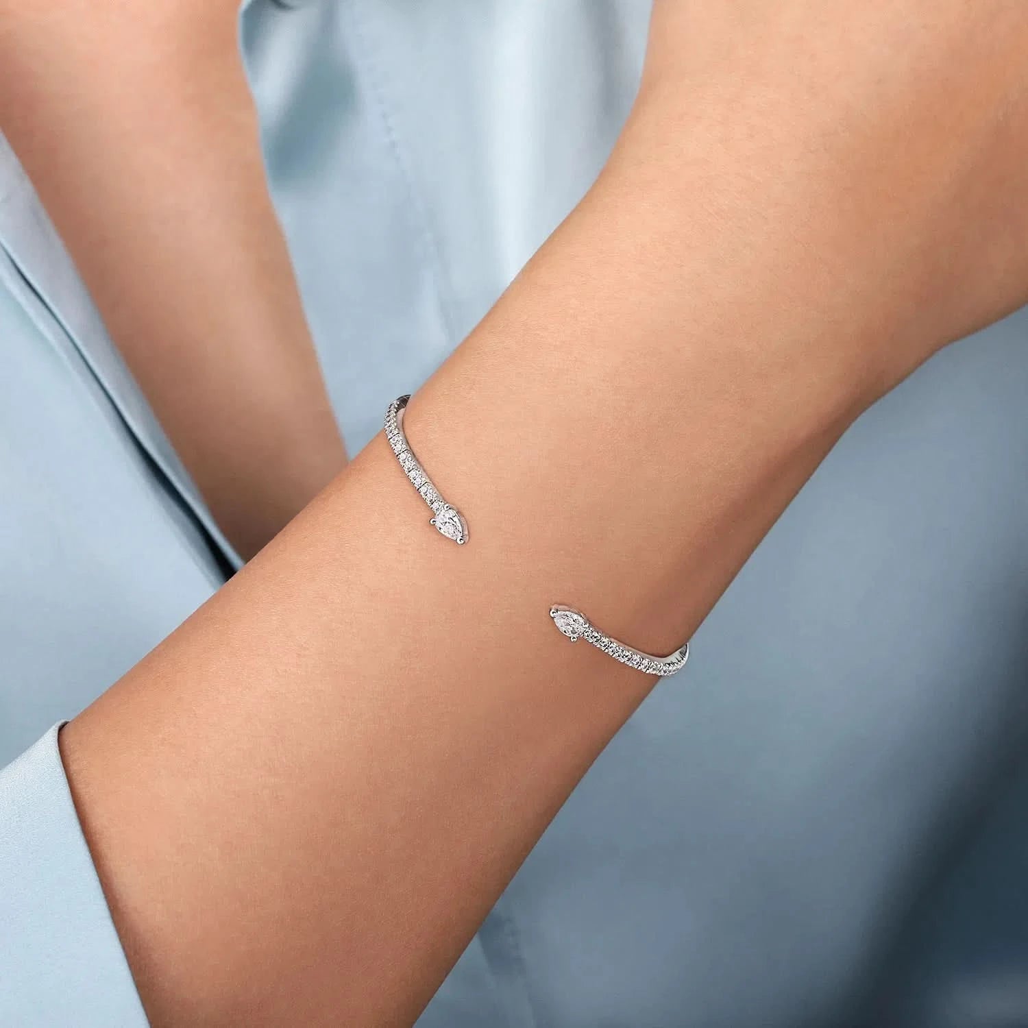 A close-up of a delicate white gold bracelet with pavé-set clear stones, worn on a person's wrist against a soft light blue shirt background.