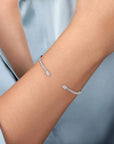 A close-up of a delicate white gold bracelet with pavé-set clear stones, worn on a person's wrist against a soft light blue shirt background.