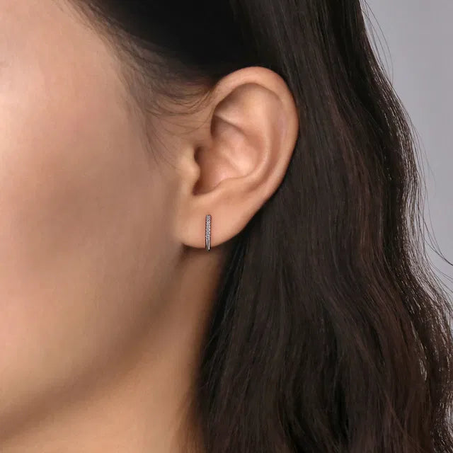 Close-up of an ear wearing a small hoop earring with dark hair and blurred background