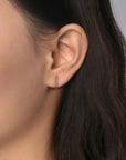 Close-up of an ear wearing a small hoop earring with dark hair and blurred background