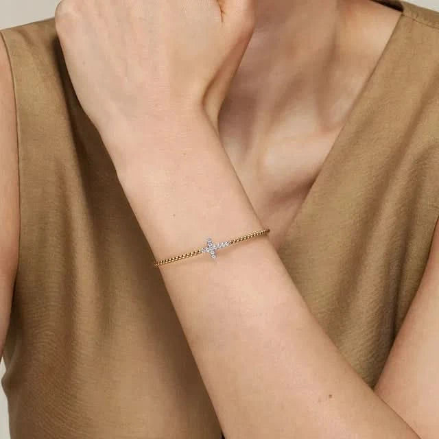 Person wearing a delicate bracelet with a cross charm on a neutral background