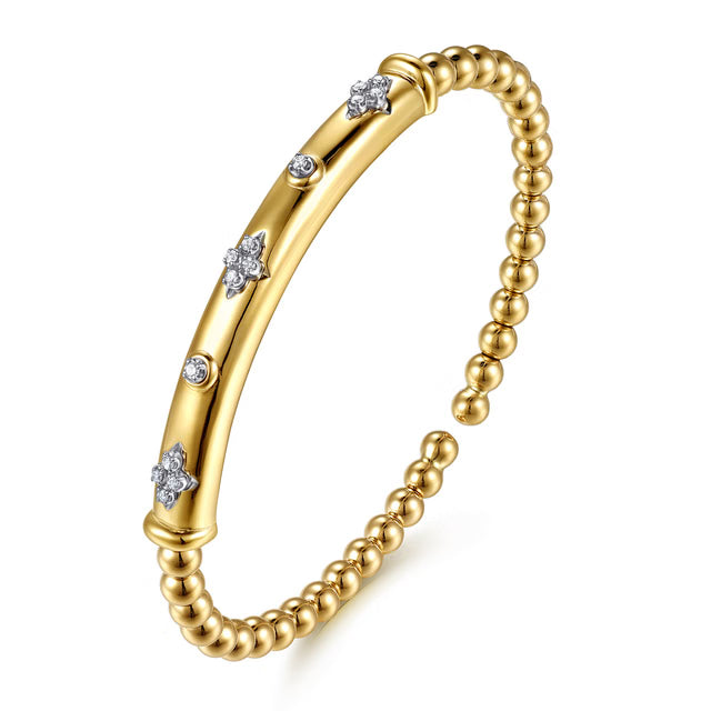 A gold cuff bangle bracelet featuring a polished central bar decorated with small star-shaped and round diamond accents, flanked by a beaded chain of gold beads, shown on a white background. angled