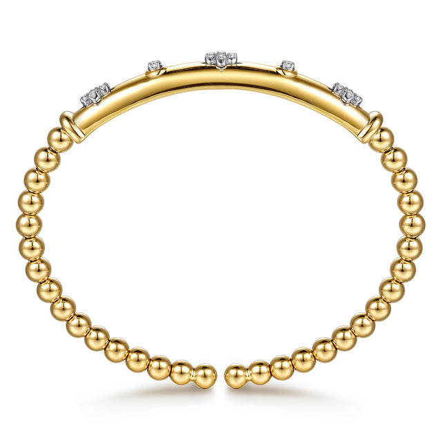 A gold bangle bracelet with a polished curved top band accented by small clear stones, and a beaded lower band made of round gold beads, shown on a white background. side view