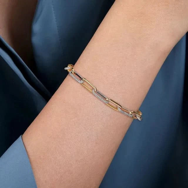 Gold bracelet with diamonds on a person's wrist against a dark blue background