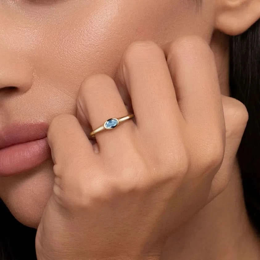 Close-up of a hand wearing a gold ring with a blue gemstone, held near the face.