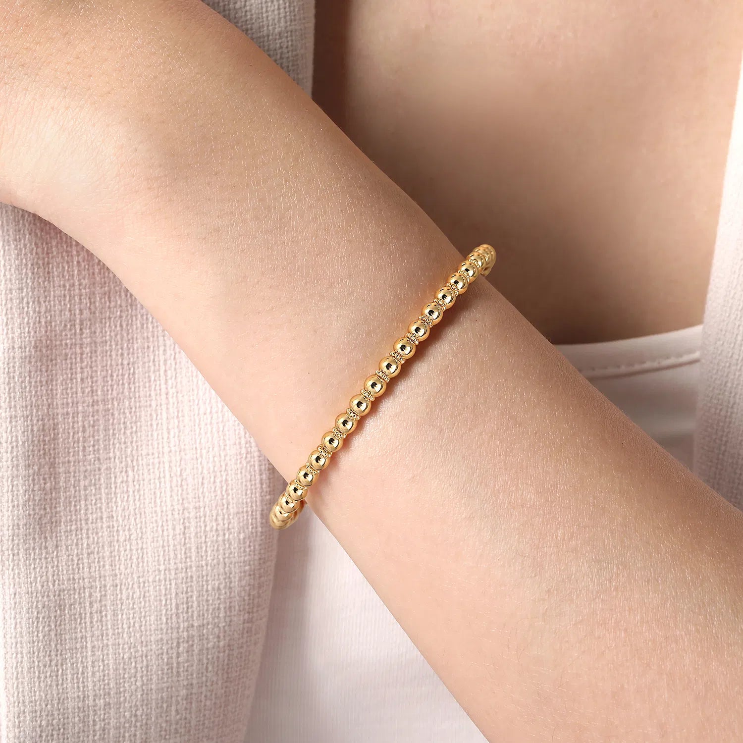 Gold beaded bracelet on a wrist with a neutral background