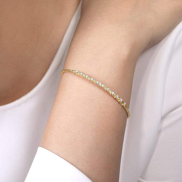 A delicate gold bracelet with small clear stones, shown worn on a person's wrist against a white top.