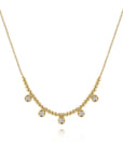A delicate gold necklace featuring a beaded chain with five small bezel-set round clear gemstones, displayed on a clean white background.