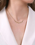 A close-up of a model wearing a delicate gold necklace with small dangling clear stones, styled with a white collared blouse.