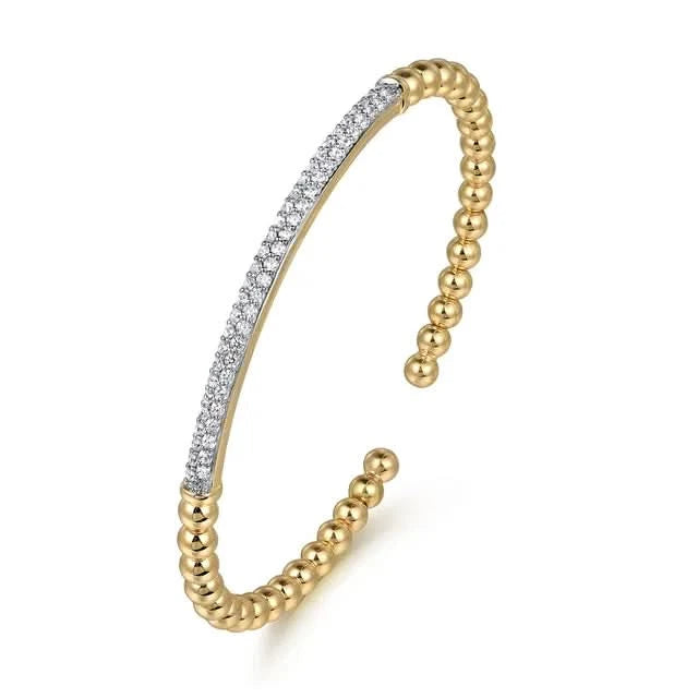 Gold bangle with diamond accents on a white background angled