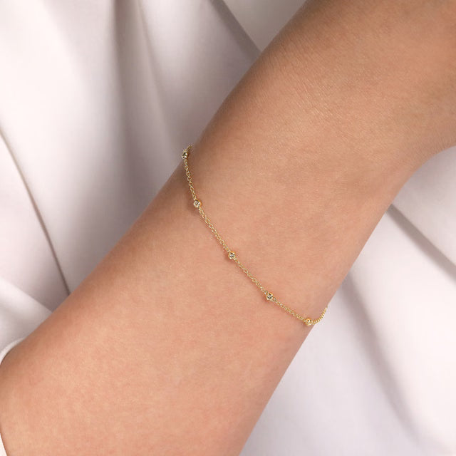 Gold bracelet with diamond stations on a person's wrist against a white background