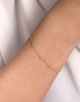 Gold bracelet with diamond stations on a person's wrist against a white background