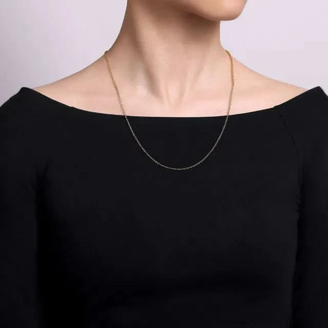 Person wearing a thin gold chain necklace against a plain background