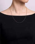 Person wearing a thin gold chain necklace against a plain background