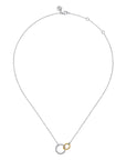 A delicate silver chain necklace featuring a pendant with two interlocking rings, one textured silver and one smooth yellow gold, displayed on a solid white background.