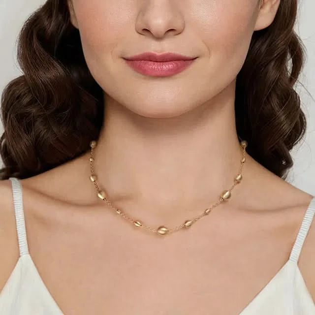 Woman wearing a gold necklace with round beads on a plain background