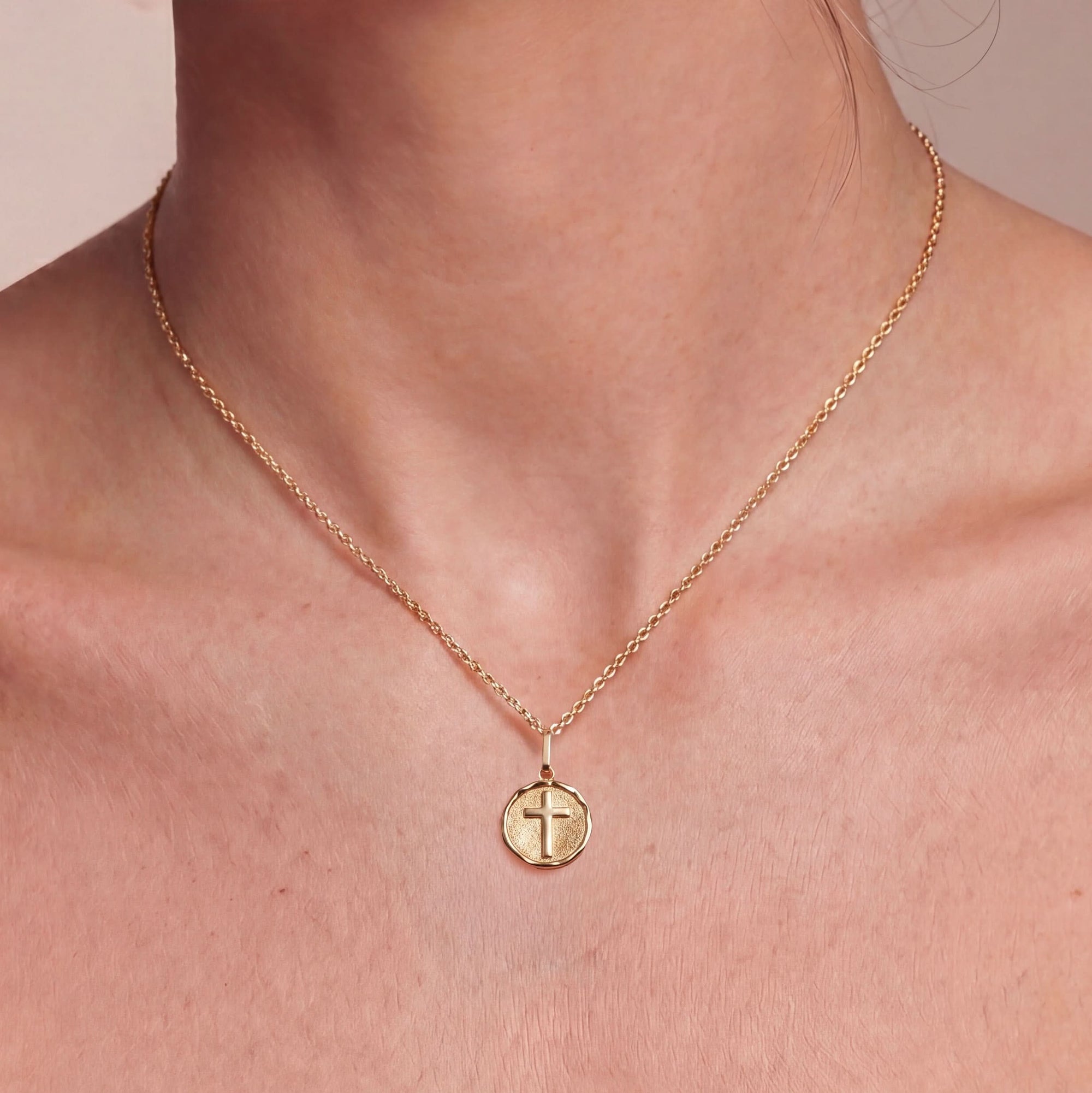 Gold necklace with a cross pendant on a person's neck against a neutral background