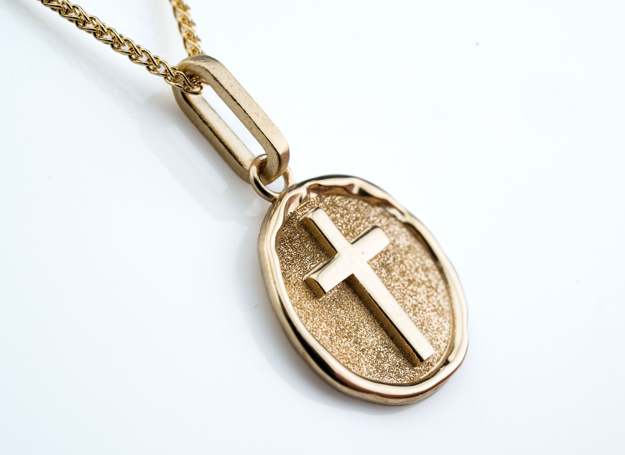 Gold pendant with a cross design tilted side profile on a white background