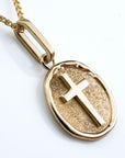 Gold pendant with a cross design tilted side profile on a white background