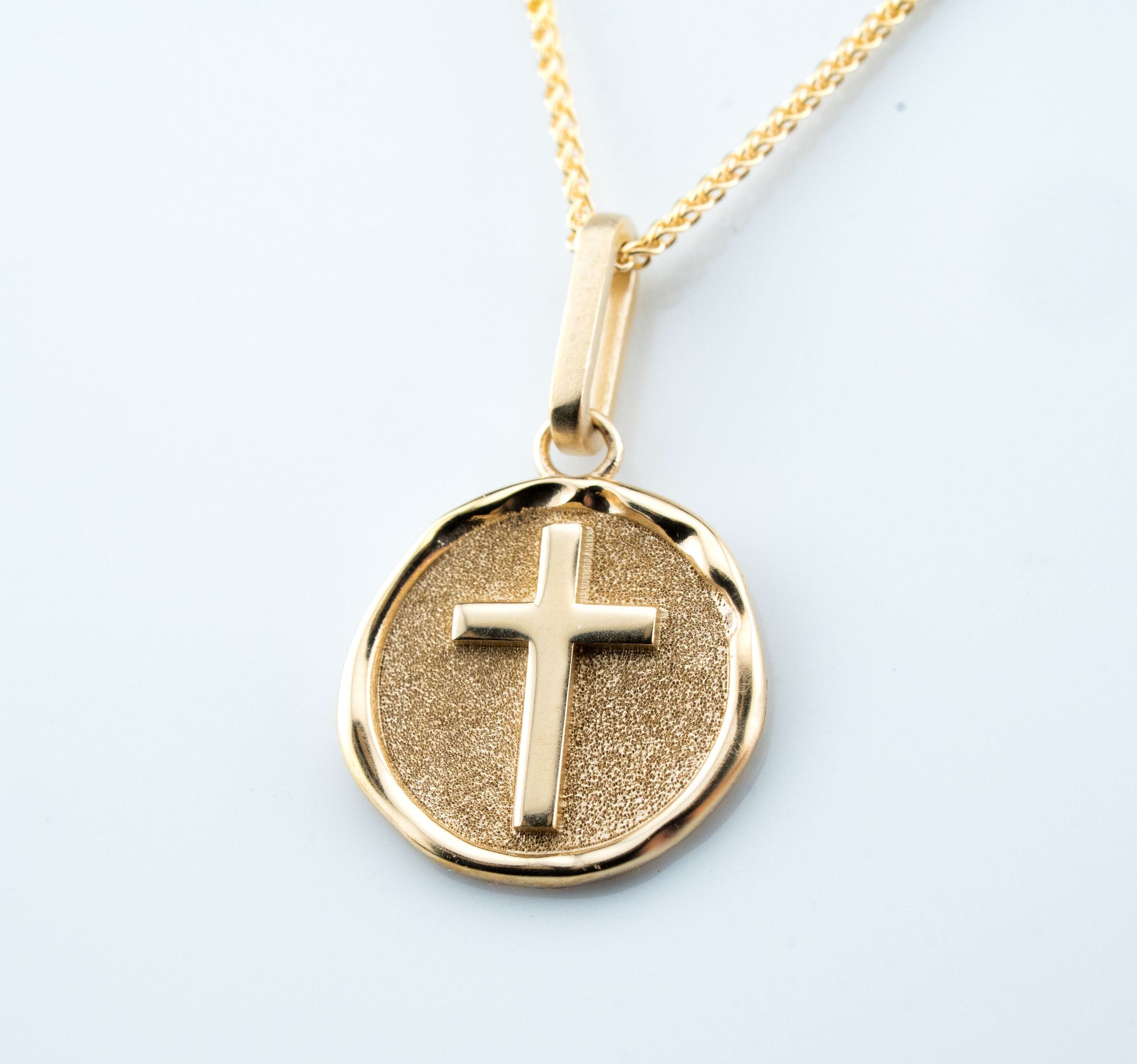 Gold necklace with a round pendant featuring a cross on a light gray background