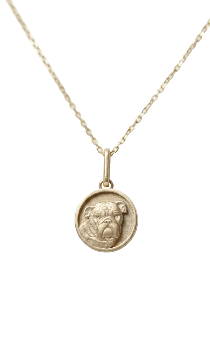 A high-relief 14k yellow gold round bulldog pendant crafted by Skeie's Jewelers, showcasing intricate facial details, a custom bone collar charm, and a matte-finish medallion face with blurred chain on a clean white background.