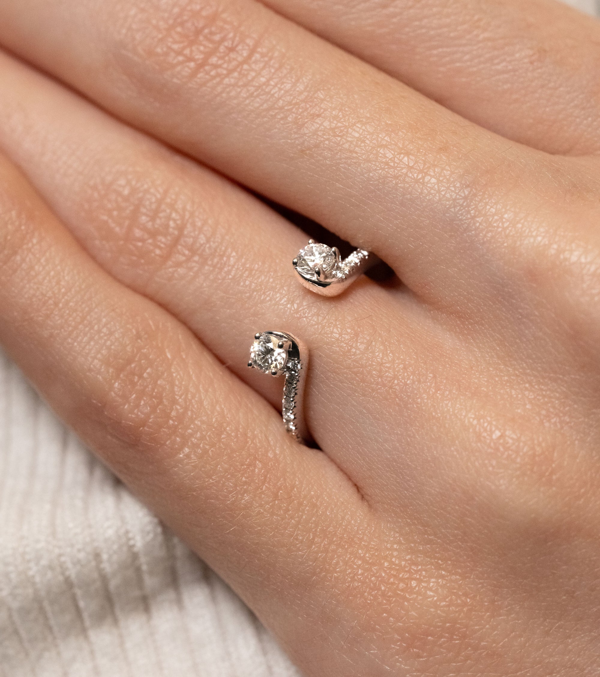 Close-up of a hand wearing an open diamond enhancer ring on a neutral background